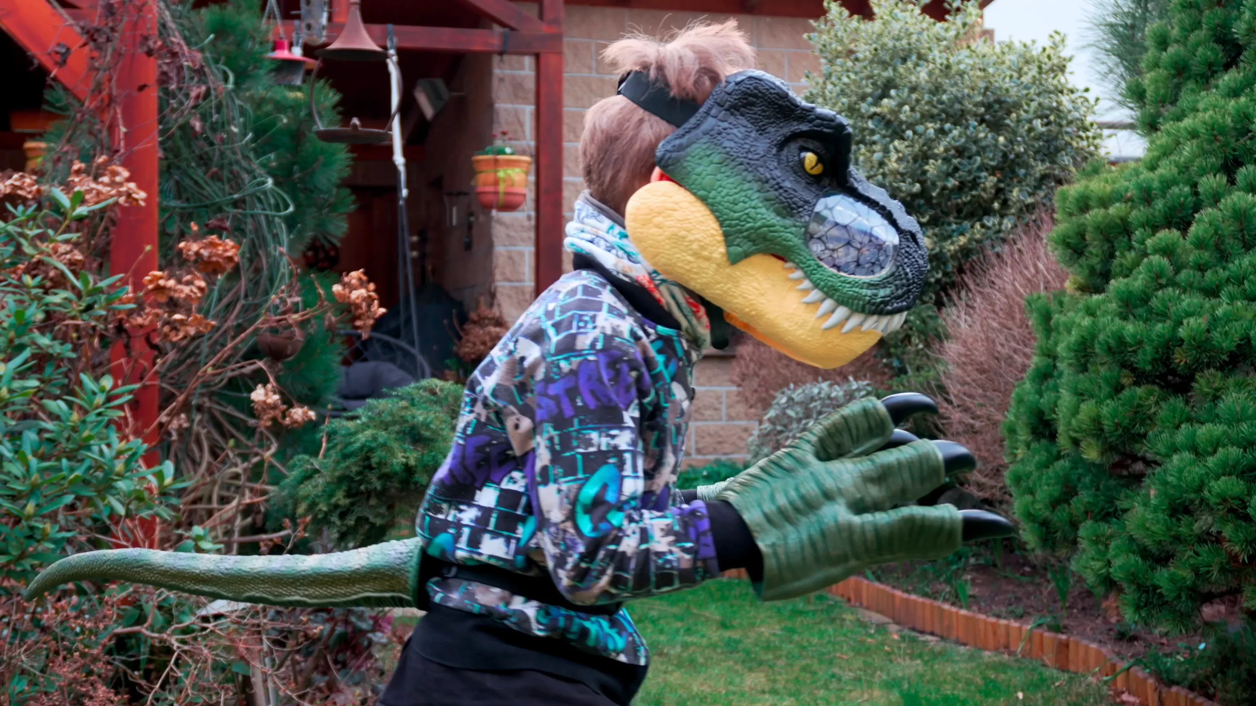 Dítě s dinosauří maskou T-Rex a drápy v zahradě